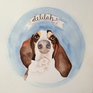 May include: Watercolour painting of a dog with brown and white fur. The dog is looking directly at the viewer. The dog's name, "Delilah", is written in cursive on a blue banner above the dog.