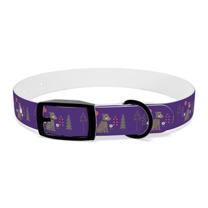 Op de afbeelding: Een paarse hondenhalsband met een herhalend patroon van grijze Schnauzer honden, groene dennenbomen, witte bloemen en kleine rode cirkels. De halsband is voorzien van een zwarte kunststof gesp en een zwarte metalen D-ring, met een witte voering.