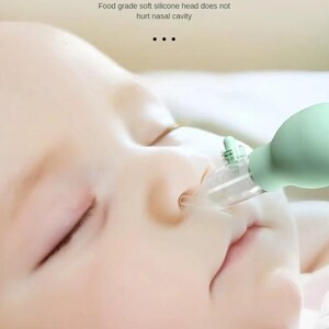 May include: A close-up of a baby's face with a green and clear nasal aspirator. The aspirator has a 15-degree bending design and a soft silicone head. Text on the image reads: "15 DEGREE BENDING DESIGN" and "Food grade soft silicone head does not hurt nasal cavity."