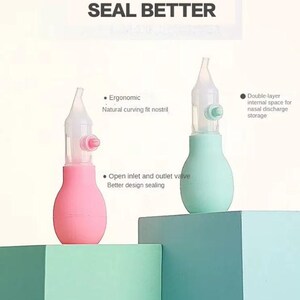 May include: Two nasal aspirators, one pink and one mint green, are displayed against a backdrop of teal and green blocks. The text "UPGRADE AND SEAL BETTER" is visible. Features include ergonomic design, open inlet/outlet valve, and double-layer internal space.
