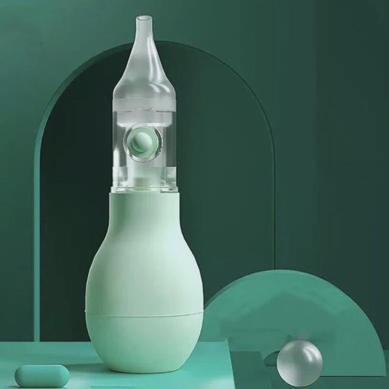 May include: A light green nasal aspirator with a clear, transparent tip and a bulb-shaped body. The aspirator has a clear chamber with a small green ball inside. A small, light green capsule is at the bottom.
