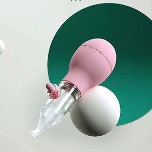 May include: A pink and clear baby nasal aspirator with the text "YOU NEED THIS TO MAKE YOUR BABY SLEEP AT EASE." The aspirator is positioned on a white sphere and a green circle. The text "Soft and comfortable", "Safe and Secure", and "Convenient and hygienic" are also present.