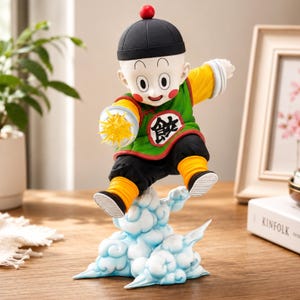 Pode incluir: Estatueta de um personagem da série de anime Dragon Ball. A figura usa uma roupa verde e preta, um chapéu preto com uma esfera vermelha e está em uma nuvem. O personagem segura uma explosão de energia amarela.