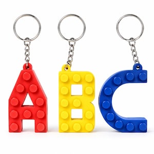 May include: Three keychains shaped like the letters A, B, and C. The letter A is red, the letter B is yellow, and the letter C is blue. Each letter features a raised stud texture on the front surface and is attached to a silver metal ring.