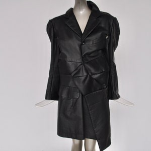 May include: A black leather jacket with a unique, asymmetrical design. The jacket has a single button closure and a collar.