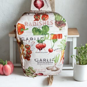 May include: A white fabric crossbody bag with a vegetable print featuring radishes, garlic, and beets. The bag has a zipper closure and a small pocket. Text on the bag includes "Radishes", "Garlic", and "Beet".