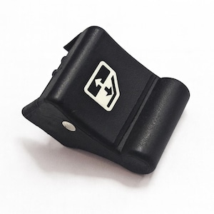 Puede incluir: Interruptor de ventana de coche de plástico negro con un símbolo de ventana y flecha blanco. El interruptor tiene un diseño curvo y un pequeño botón plateado. El botón de control de la ventana es probablemente para las ventanas eléctricas de un vehículo.