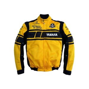 Peut inclure: Veste de course Yamaha jaune et noire. La veste présente le logo Yamaha, le texte "SEMAKIN DI DEPAN" et "50" sur le devant. Des touches de noir sont présentes sur les manches et les épaules.