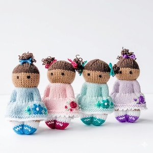 May include: Four small, hand-knitted dolls with brown yarn hair styled in buns with small bows. Each doll wears a dress in pastel blue, pink, mint green, or lavender, featuring embroidered floral details at the hem and white knitted shoes.
