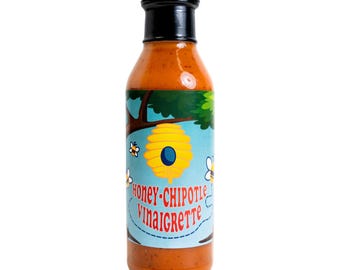 May include: A clear glass bottle filled with orange liquid, topped with a black cap. The label features a light blue background with a yellow beehive, small bees, and the red text "HONEY-CHIPOTLE VINAIGRETTE" printed in a stylized font.