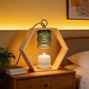 May include: A wooden hexagonal candle holder with a green glass lamp and a white candle. The candle is lit and has the text "SILK SMELL" on it. The lamp is suspended from a gold ring.