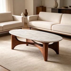 Puede incluir: Mesa de centro ovalada con tapa de mármol blanco y base de madera oscura. La base tiene un diseño curvo único. La mesa está en un salón con muebles de colores neutros y una alfombra.