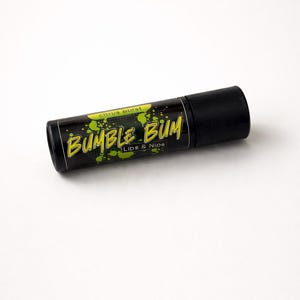 Puede incluir: Un tubo de bálsamo labial negro con el texto "BUMBLE BUM" en amarillo, contorneado en blanco, y las palabras "Lips & Nips" debajo. Las palabras "Citrus Burst" están encima del texto principal. Salpicaduras de pintura verde están en el tubo.