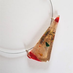 Peut inclure: Un collier composé d'un pendentif triangulaire en verre translucide suspendu à un fin tour de cou en fil métallique argenté. Le pendentif présente des éclats incrustés rouges, verts, jaunes et noirs, avec des accents en verre rouge aux extrémités.