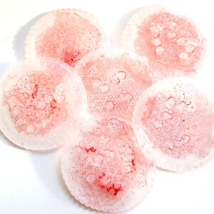 May include: Six round, translucent, white coasters with a pink, speckled, marbled design.