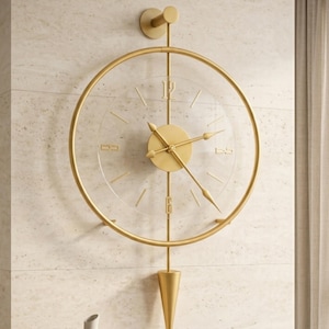Könnte beinhalten: Eine goldfarbene, moderne Wanduhr mit transparentem Zifferblatt und römischen Ziffern. Die Uhr hat ein kreisförmiges Design mit Pendel und ist an einer hellen Wand befestigt. Eine weiße Vase und Bücher stehen auf einem Holztisch darunter.