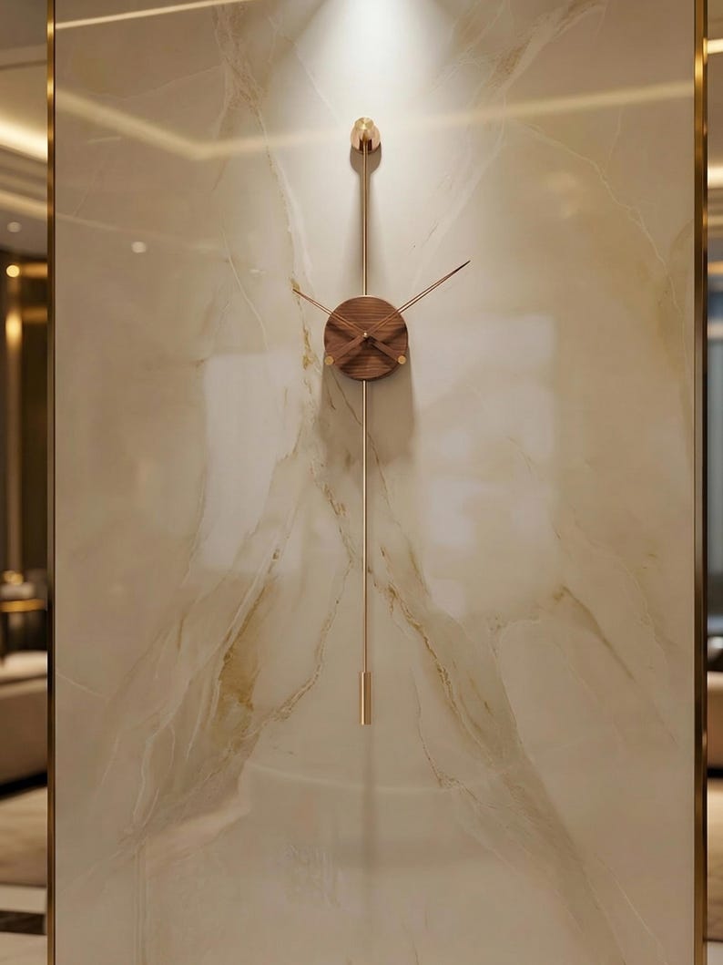 May include: A modern wall clock with a minimalist design. The clock features a round, wooden face with thin, gold-colored hands and a pendulum. The clock is mounted on a marble-like wall.