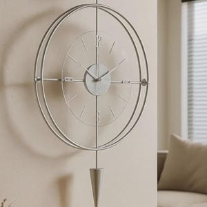 Pode incluir: Um relógio de parede moderno e minimalista em cinza claro. O relógio apresenta um design circular com um mostrador de vidro transparente e um pêndulo. Os ponteiros e os marcadores de hora são simples e elegantes, criando uma estética limpa.
