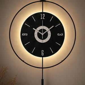 May include: A modern wall clock with a black face and white numerals. The clock is surrounded by a black metal ring and has a pendulum. The clock face is illuminated with a warm light, creating a stylish and contemporary design.