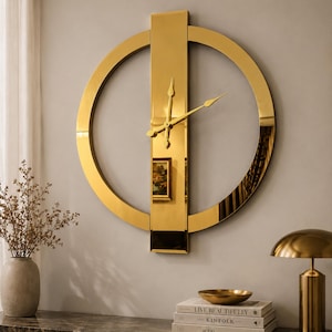 May include: A gold-colored wall clock with a circular design and a vertical rectangular bar. The clock hands are black. The clock is mounted on a light gray wall. The clock is a decorative home decor item.