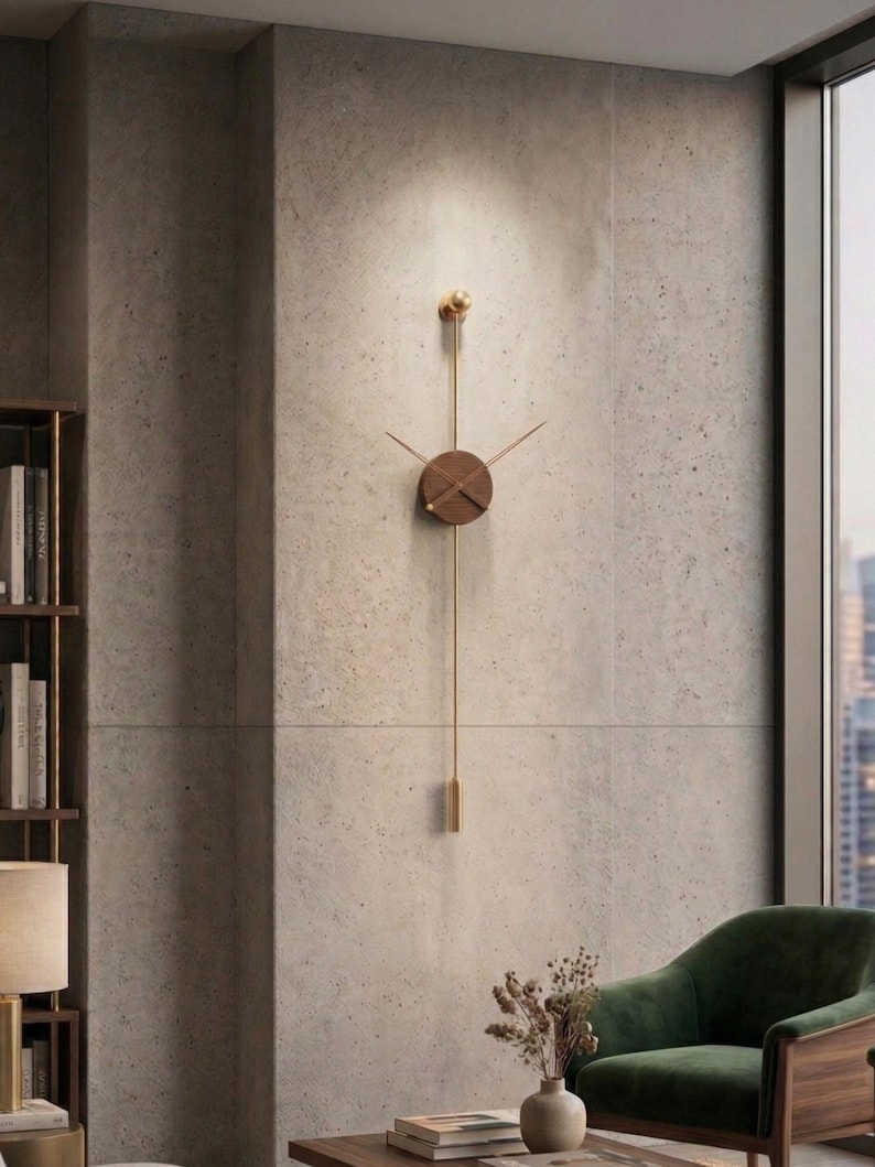 May include: A modern wall clock with a minimalist design. The clock features a round, dark wood face with gold-colored hands and a long, gold pendulum. The clock is mounted on a textured, light gray wall.