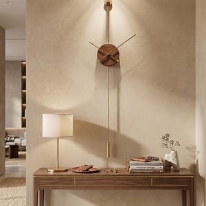 May include: A modern wall clock with a wooden face and gold-colored accents. The clock has a long pendulum and is mounted on a beige wall. A wooden console table with a lamp and decorative items is below the clock.