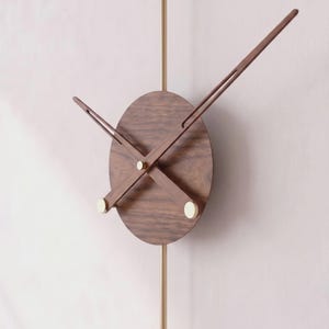 May include: A modern wall clock with a round, dark wood face and slender wooden hands. The clock features a brass pendulum and small, gold-colored accents. The hands are positioned to indicate the time.
