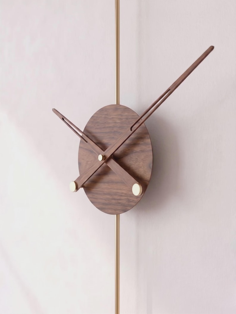 May include: A modern wall clock with a round, dark wood face and slender wooden hands. The clock features a brass pendulum and small, gold-colored accents. The hands are positioned to indicate the time.