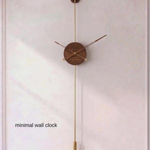 May include: A minimalist wall clock with a wooden face and brass accents. The clock is 31.5 inches in length and features a long pendulum. The text "STATEMENT SIZE 80 cm | 31.5" is visible. The words "minimal wall clock" are also visible.