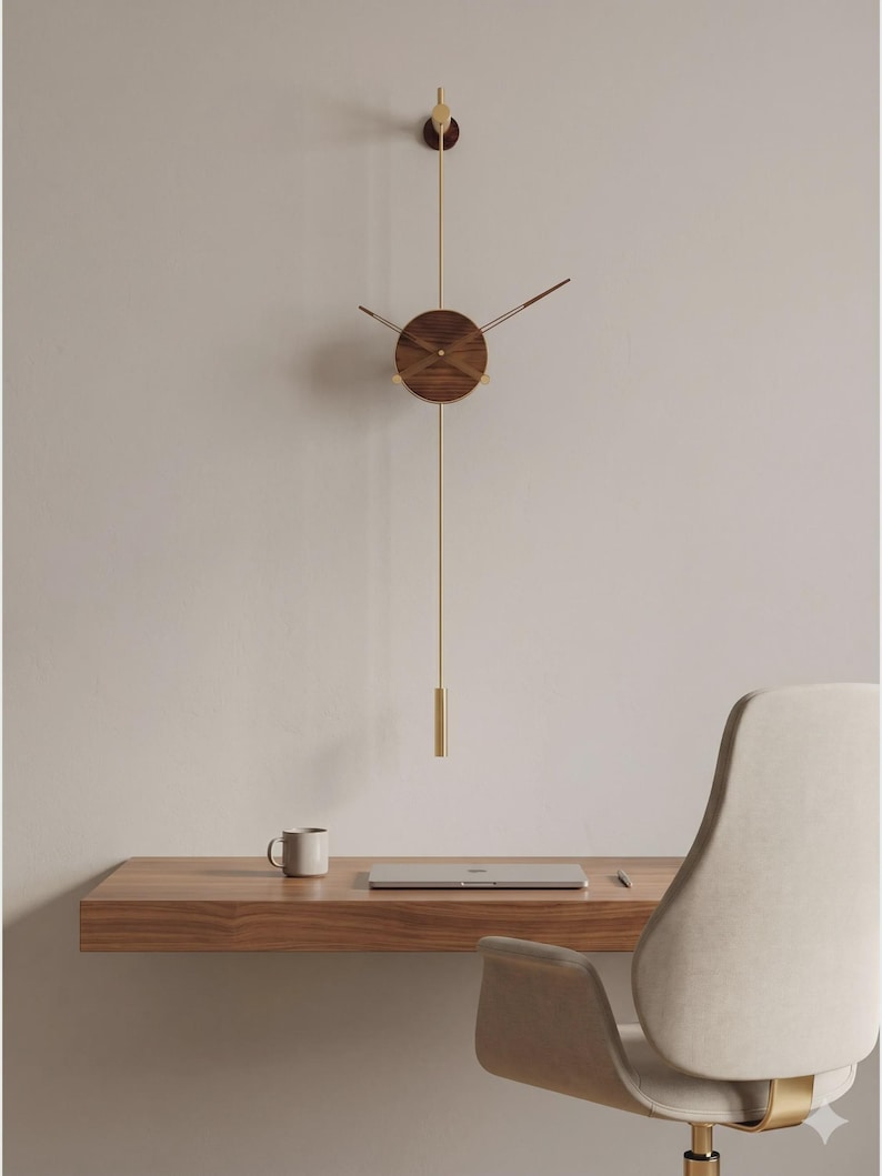 May include: A modern wall clock with a round, wooden face and brass hands and pendulum. The clock hangs on a light-colored wall above a wooden desk with a laptop and mug. The clock's design is minimalist and elegant.