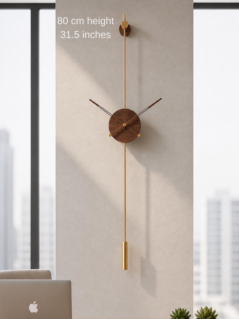 May include: A modern wall clock with a walnut wood face and hands, suspended by a gold-colored rod. The clock is 31.5 inches in height and features a minimalist design. The clock is mounted on a neutral-colored wall.