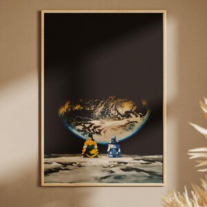 May include: A rectangular wall art print featuring two figures sitting on a rocky, cratered lunar surface. They are looking up at a large, glowing Earth suspended in the dark, vast expanse of space. The print is encased in a light wood frame.