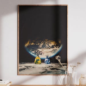 May include: A rectangular wall art print featuring two figures sitting on a cratered lunar surface, looking up at a glowing, partially illuminated Earth against a deep black space background. The figures wear yellow and blue jackets.