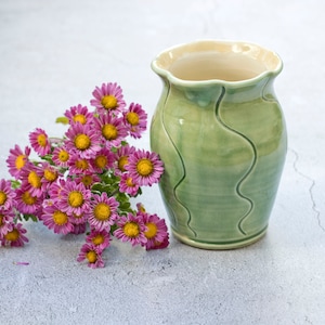 May include: A green ceramic vase with a wavy design, filled with a bouquet of pink flowers.
