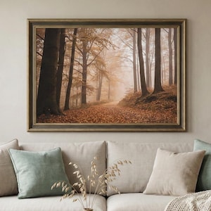 May include: A framed print shows a forest scene with tall trees and a path covered in fallen leaves. The artwork has a warm colour palette of browns and oranges, creating a cosy atmosphere. The print is displayed above a beige sofa.