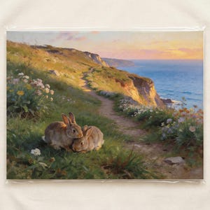 May include: A print of a landscape painting showing two brown rabbits in grass near a coastal path. The path winds along a cliff with the sea in the background. The sky is a blend of orange and blue.