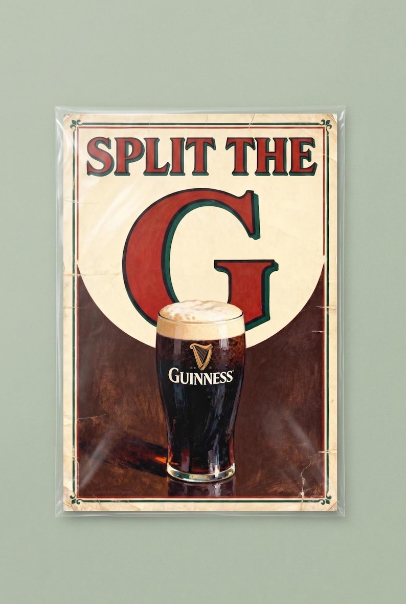 May include: A framed Guinness advertisement with the text "SPLIT THE G" in red letters. A pint of Guinness stout with a creamy head is in the center. The background is a dark brown color.