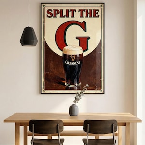 May include: A framed Guinness advertisement with the text "SPLIT THE G" and a pint of Guinness. The poster is displayed above a wooden table with two chairs. A black pendant light hangs above the table.
