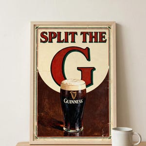 May include: Vintage-style framed print featuring a pint of Guinness stout. The artwork includes the text "SPLIT THE G" in red and green, with a creamy white head on the dark beer. A white mug sits on a wooden surface.