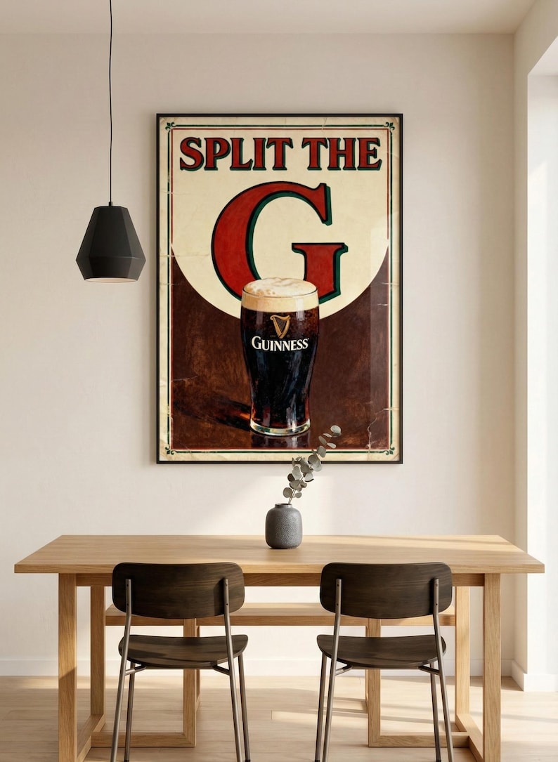 May include: A framed Guinness advertisement with the text "SPLIT THE G" above a pint of Guinness. The poster is displayed above a wooden table with two chairs. A black pendant light hangs above the table.