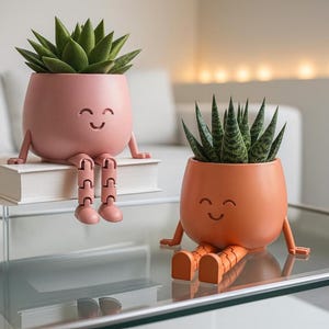 Peut inclure: Deux pots de plantes succulentes fantaisistes. L'un est rose et assis sur un livre, l'autre est orange. Les deux ont des visages souriants et des jambes articulées. Les pots sont remplis de plantes succulentes vertes.