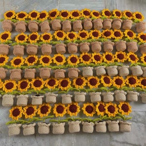 May include: A collection of handmade crochet sunflowers and potted plants. The sunflowers have yellow petals and brown centers. The potted plants are in various shades of brown and beige, creating a cheerful, handcrafted display.