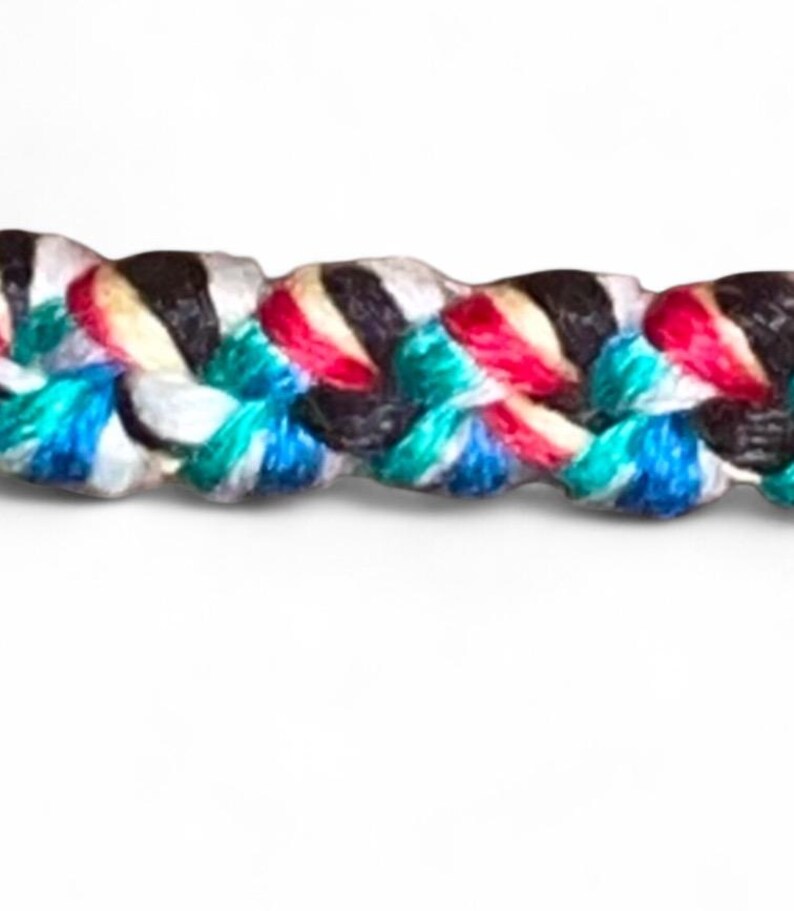May include: Close-up of a braided rope with a vibrant mix of colors. The rope features strands of black, white, red, turquoise, and blue, creating a textured and visually appealing pattern. The background is plain white.