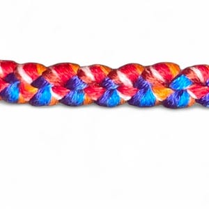 May include: Close-up of a braided rope with vibrant colors. The rope features a pattern of red, orange, blue, and white strands, creating a visually appealing texture. The rope is set against a plain white background.