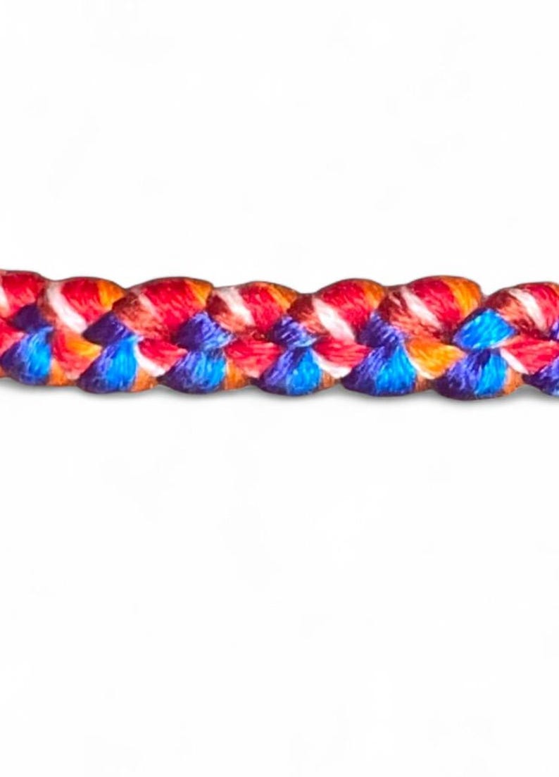 May include: Close-up of a braided rope with vibrant colors. The rope features a pattern of red, orange, blue, and white strands, creating a visually appealing texture. The rope is set against a plain white background.