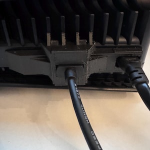 May include: Close-up of the back of a black electronic device with a series of vertical fins for heat dissipation. A black HDMI cable is plugged into the device, with the words "HDMI CABLE" and "SPEED" printed on the cable.