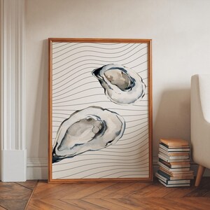 May include: Watercolor print of two oyster shells in a wooden frame. The shells are painted in shades of gray and beige, set against a background of wavy black lines on a cream-colored canvas. The frame is a warm, natural wood tone.