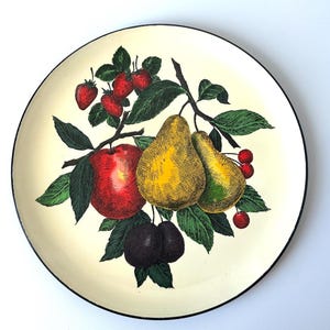 Puede incluir: Plato decorativo redondo con fondo crema y borde negro. El plato presenta una colorida ilustración de frutas, incluyendo una manzana roja, peras amarillas, fresas, cerezas y ciruelas, con hojas verdes.