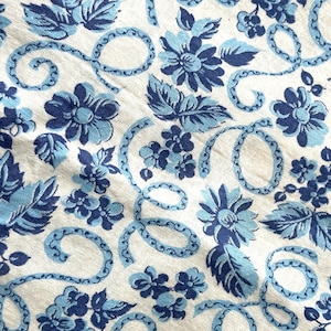 Könnte beinhalten: Nahaufnahme eines Stoffes mit einem sich wiederholenden Blumenmuster. Das Design zeigt blaue Blumen und Blätter auf hellem Hintergrund. Dekorative blaue Wirbel und Akzente tragen zur Vintage-Ästhetik bei.