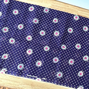 Peut inclure: Un tissu bleu fonc&eacute; avec un motif r&eacute;p&eacute;t&eacute; de marguerites blanches &agrave; centres roses et de petits pois blancs. Le tissu est probablement en coton ou dans une mati&egrave;re similaire, adapt&eacute; aux projets de couture ou de d&eacute;coration int&eacute;rieure.